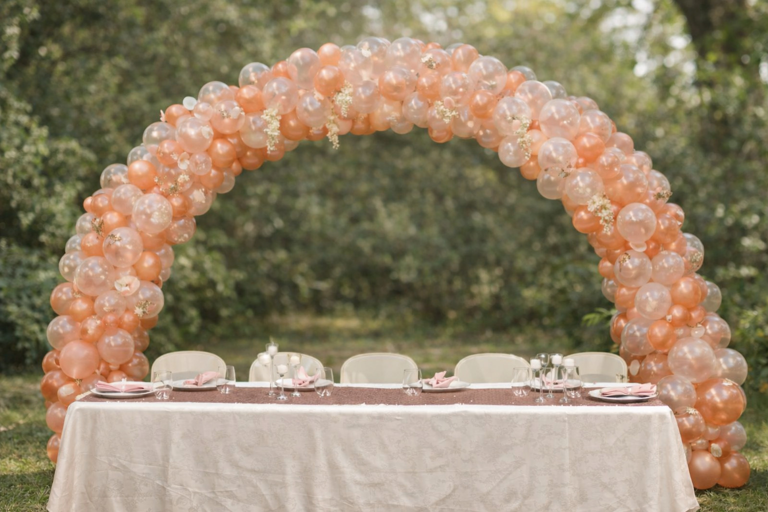 Peach and blush balloon arch built over the head table for an outdoor wedding